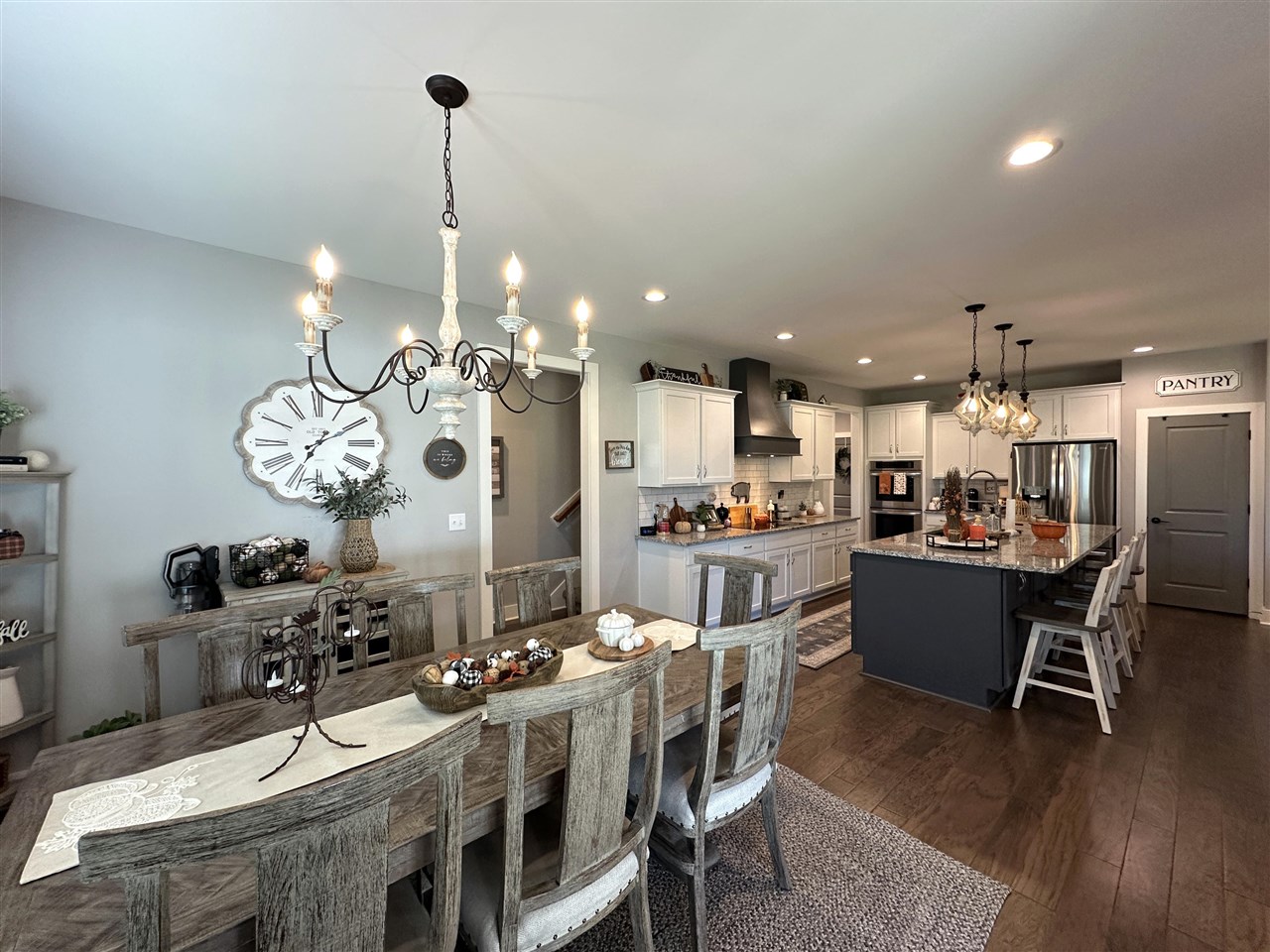 Open-plan kitchen and dining room with white cabinets, a dark island, and a long rustic wood table.