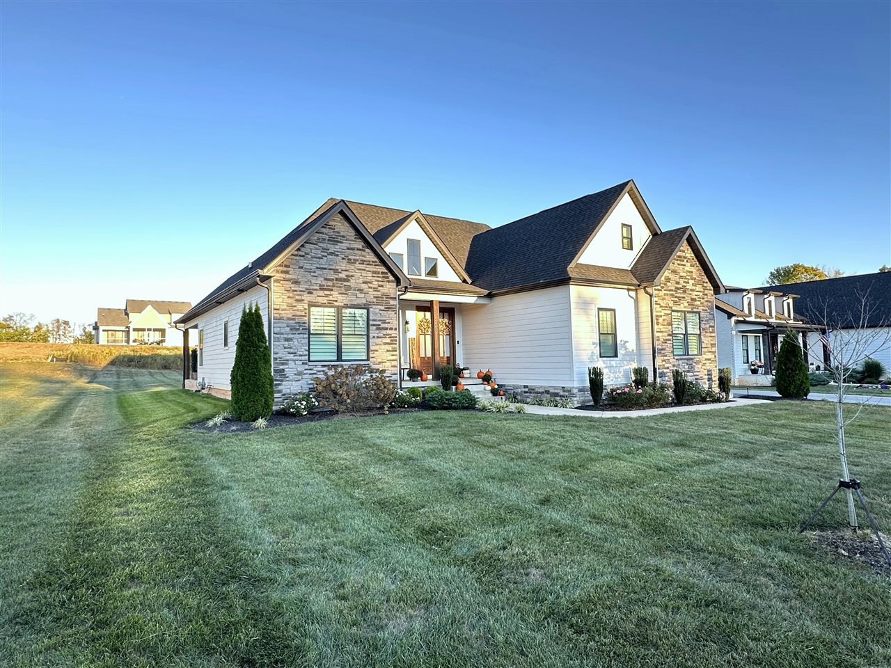 White-sided home with stone accents, multiple gables, and pumpkins at the front entrance.