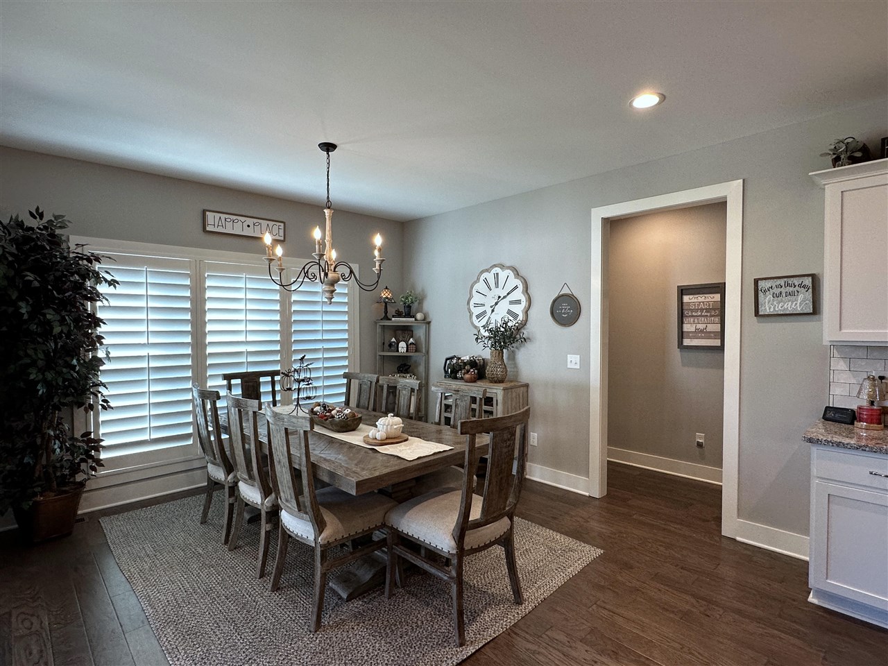 Dining room with a rustic wood table, chandelier, and white plantation shutters.