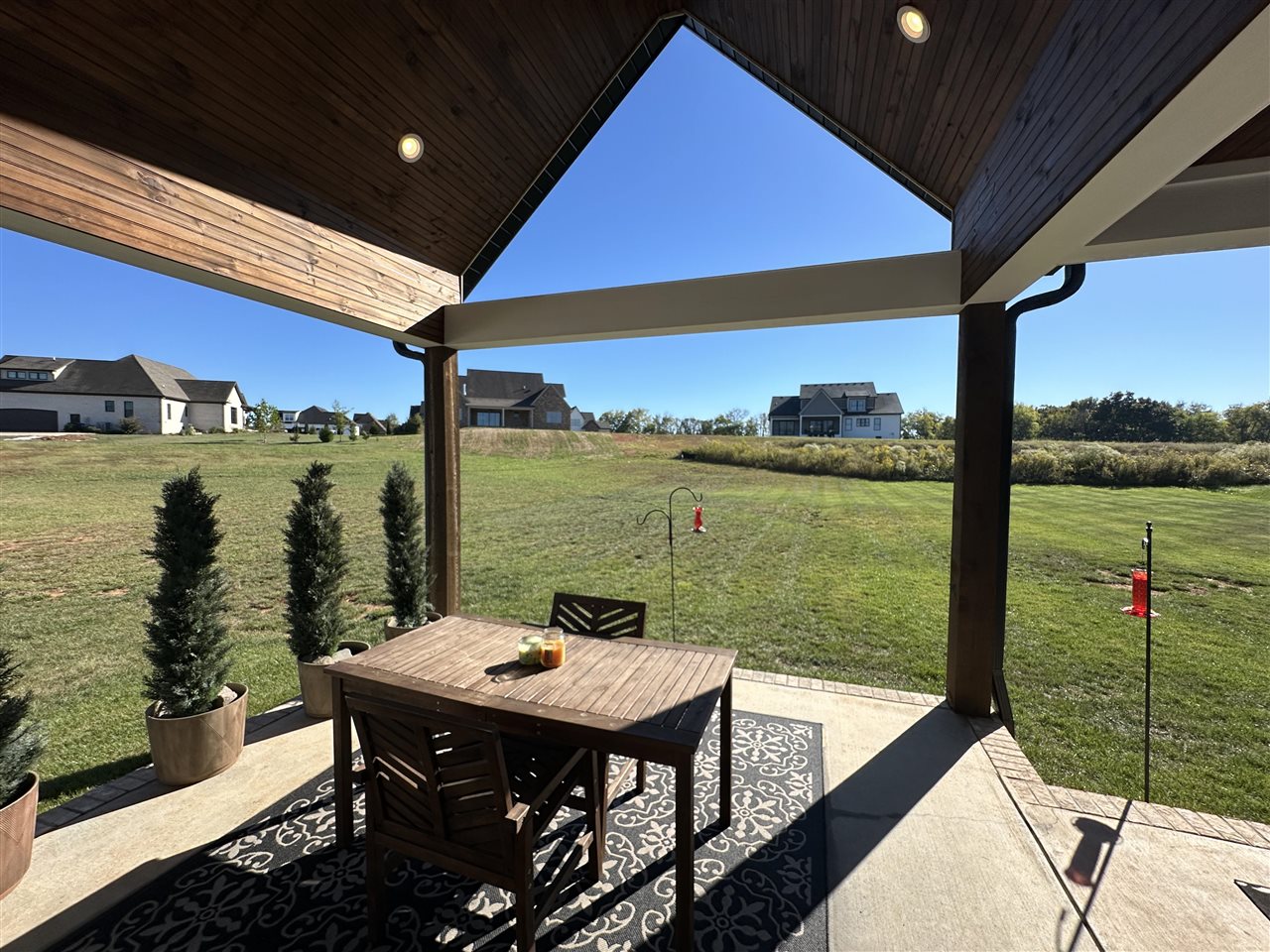 Covered patio with a wooden dining table overlooking a broad lawn and neighboring homes.