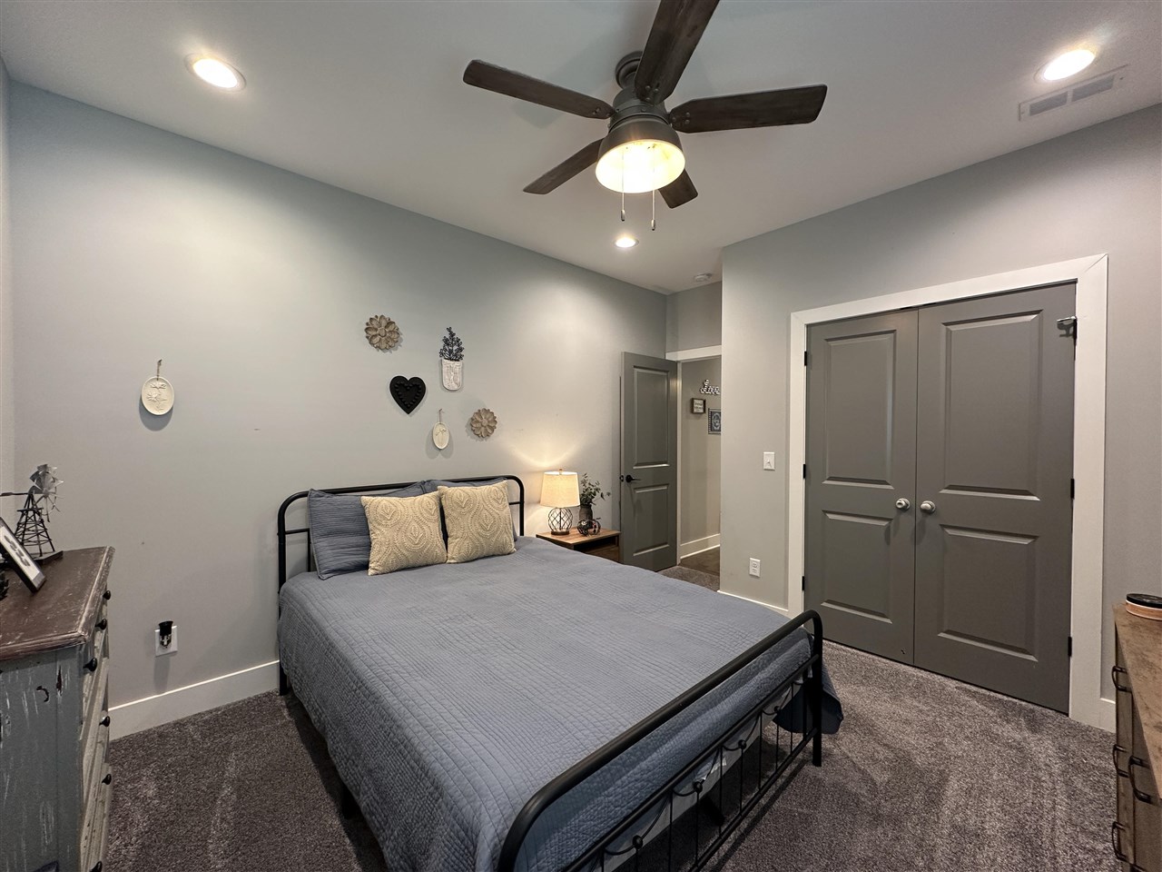 Bedroom with a gray quilted bed, gray double closet doors, and a dark ceiling fan.