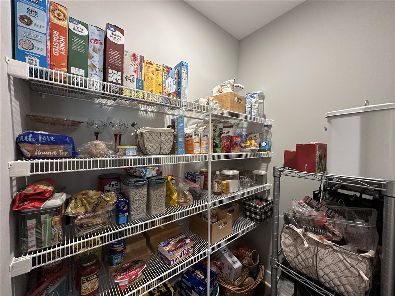Walk-in pantry with food-filled wire shelves beside a large white chest freezer.