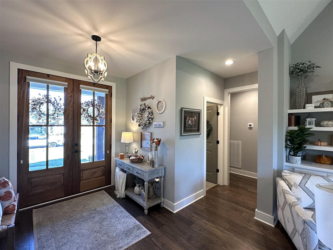Foyer with wood-and-glass double doors, a chandelier, console table, and dark wood floors.