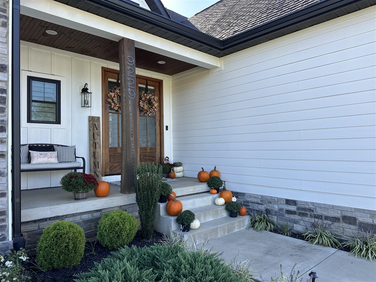 Home’s covered front porch with a wood door, stone steps, and autumn pumpkins and mums.