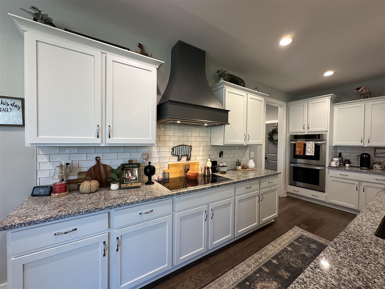 Kitchen with white cabinets, granite counters, subway-tile backsplash, and a large stainless-steel range hood.