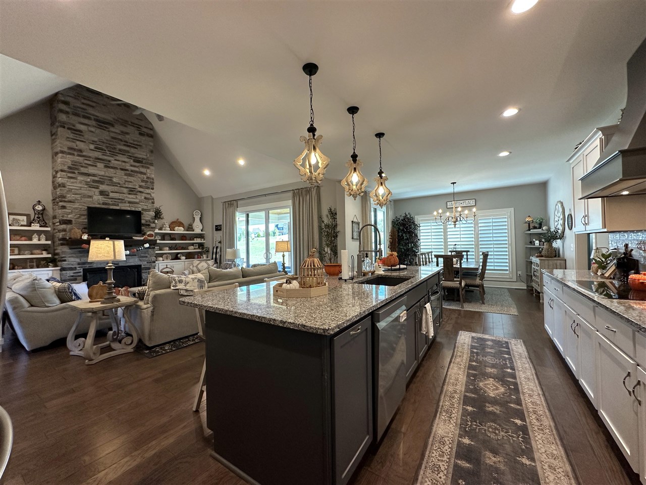 Open kitchen and living area with a granite island, vaulted ceiling, and stone fireplace.