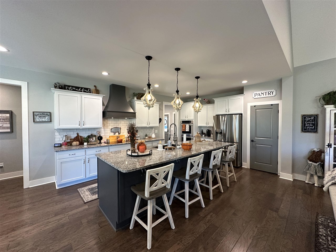 Kitchen with white cabinetry, stainless appliances, and a large granite island with four stools.