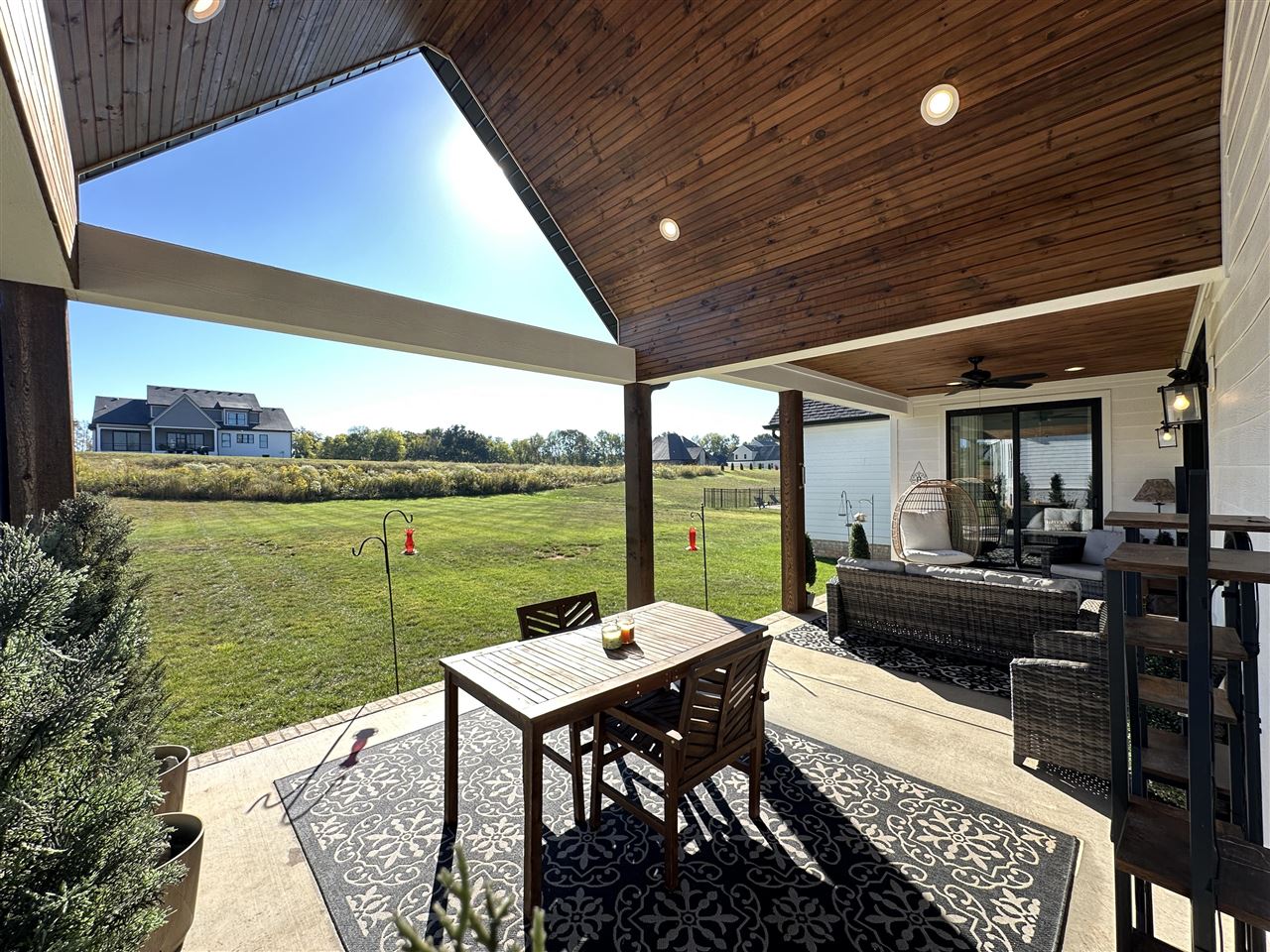 Covered patio with a vaulted wood ceiling, outdoor dining set, wicker seating, and views across the lawn.