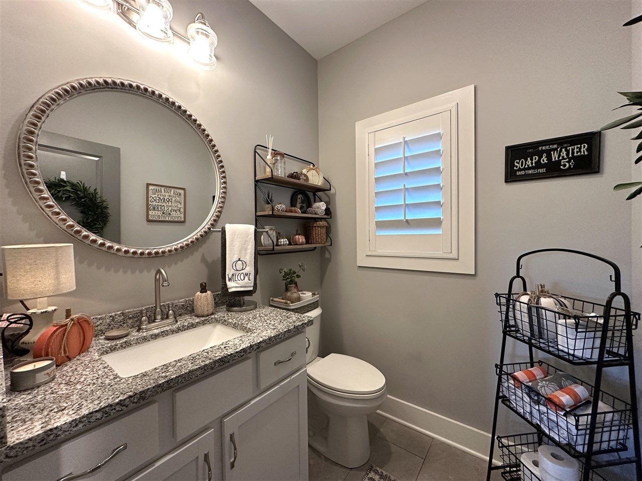 Bathroom with a granite vanity, oval mirror, toilet, and white plantation shutters.