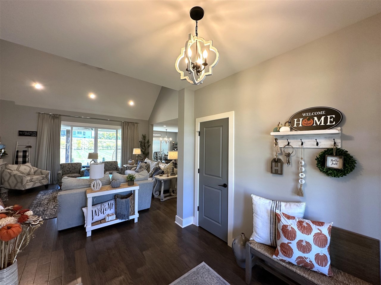 Staged living room with vaulted ceiling, chandelier, gray sectional, and pumpkin-patterned pillows.