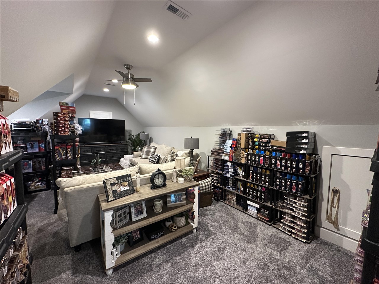 Attic bonus room with sloped ceilings, sofas, a television, and shelves of collectibles.