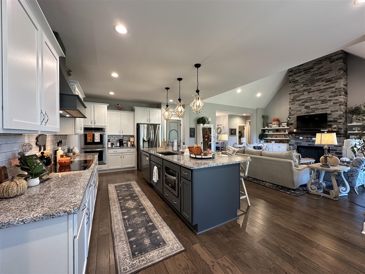Open-plan kitchen with a granite-topped island, white cabinetry, and a stone fireplace in the adjoining living room.