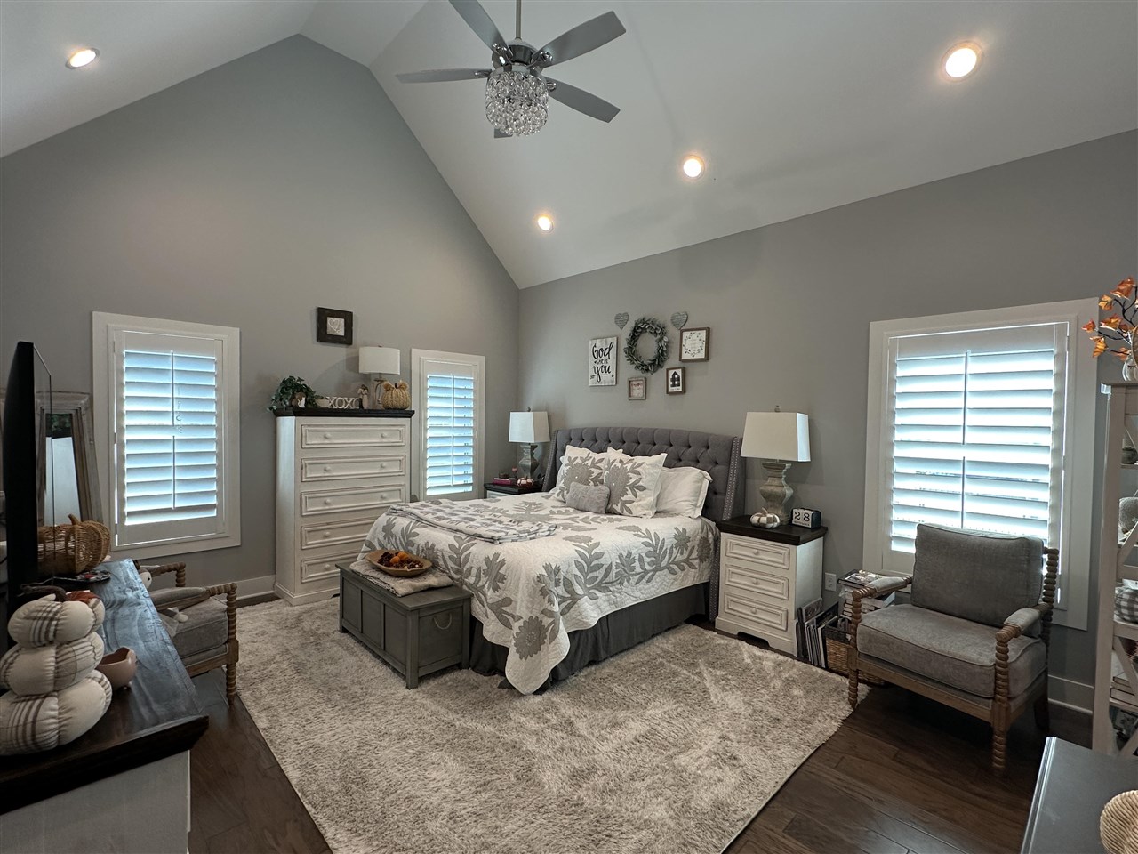 Primary bedroom with a tufted bed beneath a vaulted ceiling, plantation shutters, and a crystal ceiling light.
