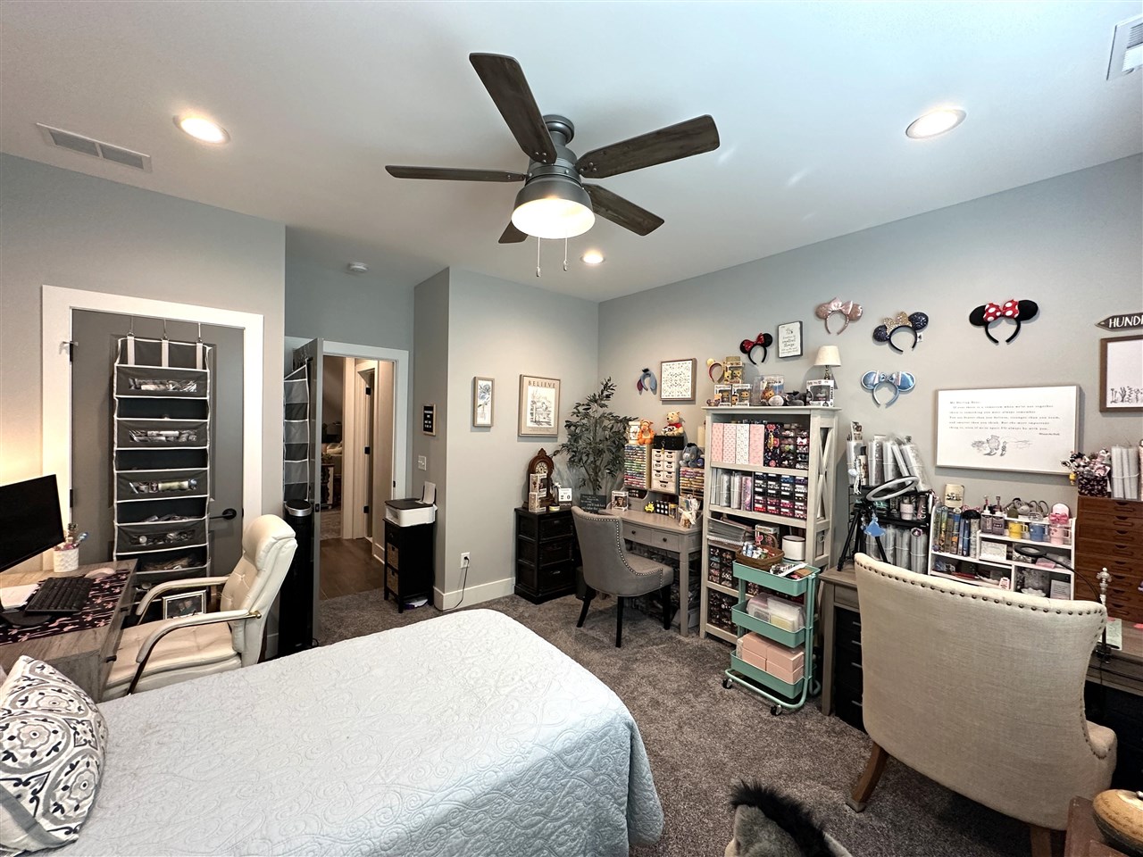 Bedroom with a ceiling fan, bed, and an extensive craft workstation along the wall.