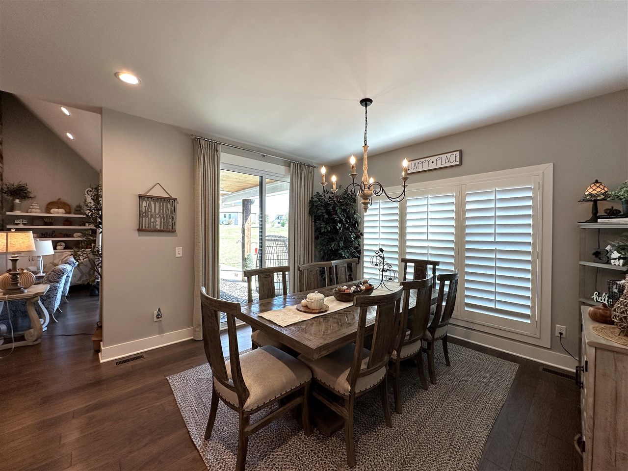 Dining room with a dark wood table, chandelier, white shutters, and glass doors to a covered patio.