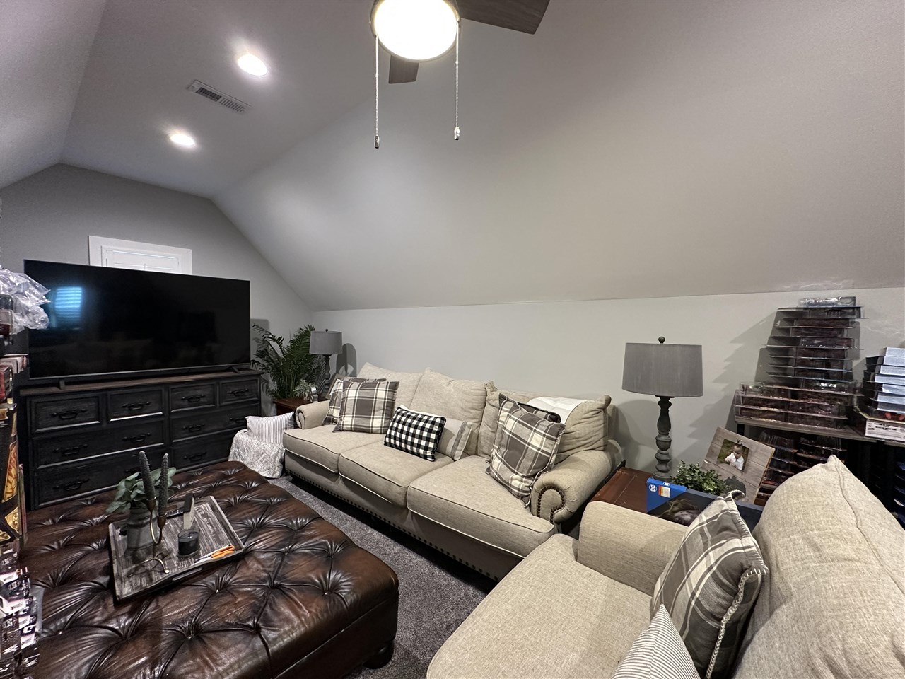 Furnished living room with a high sloped ceiling, beige sofas, and a large television.