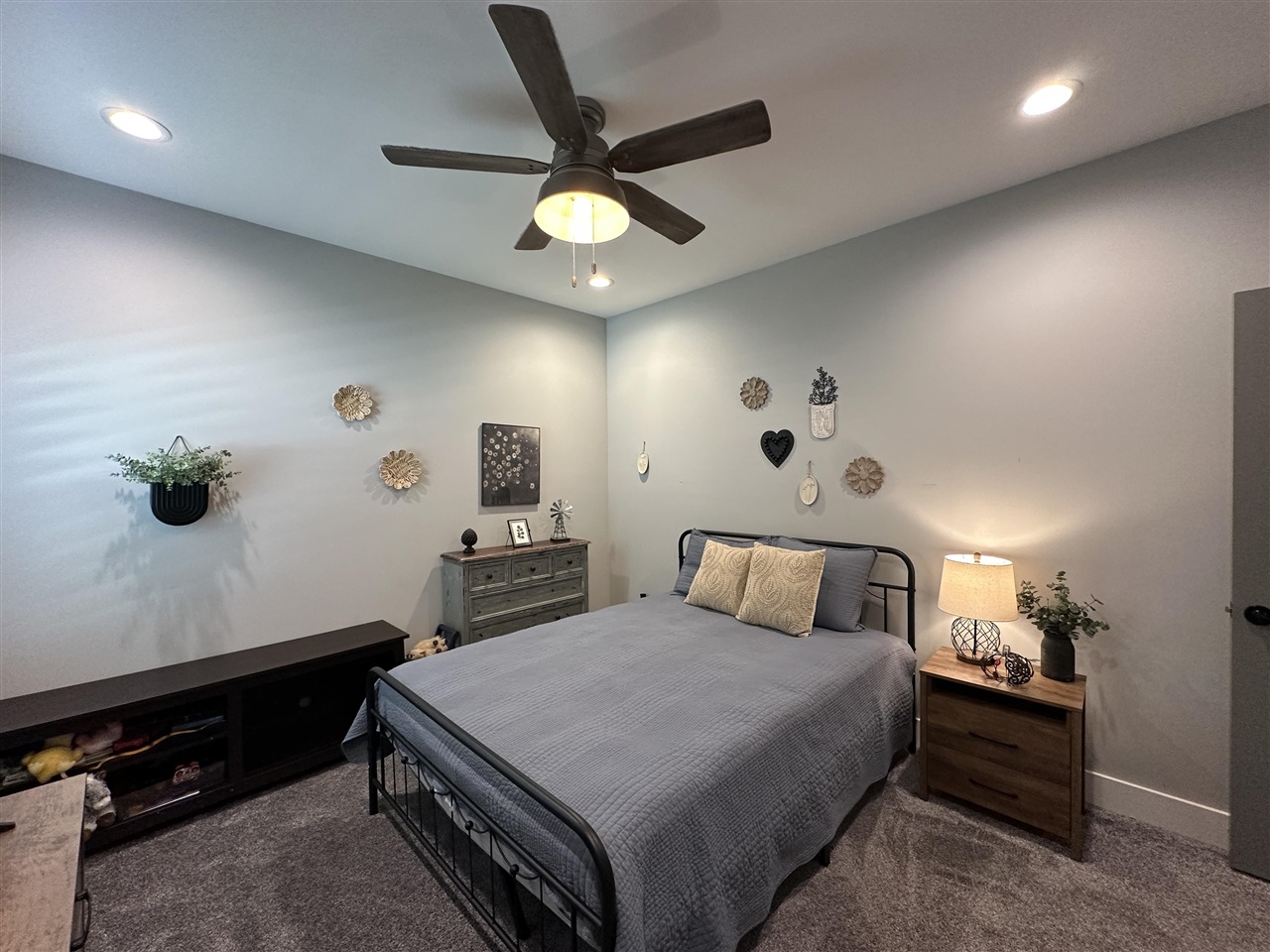 Furnished bedroom with a gray bed, black metal frame, ceiling fan, and bedside lamp.