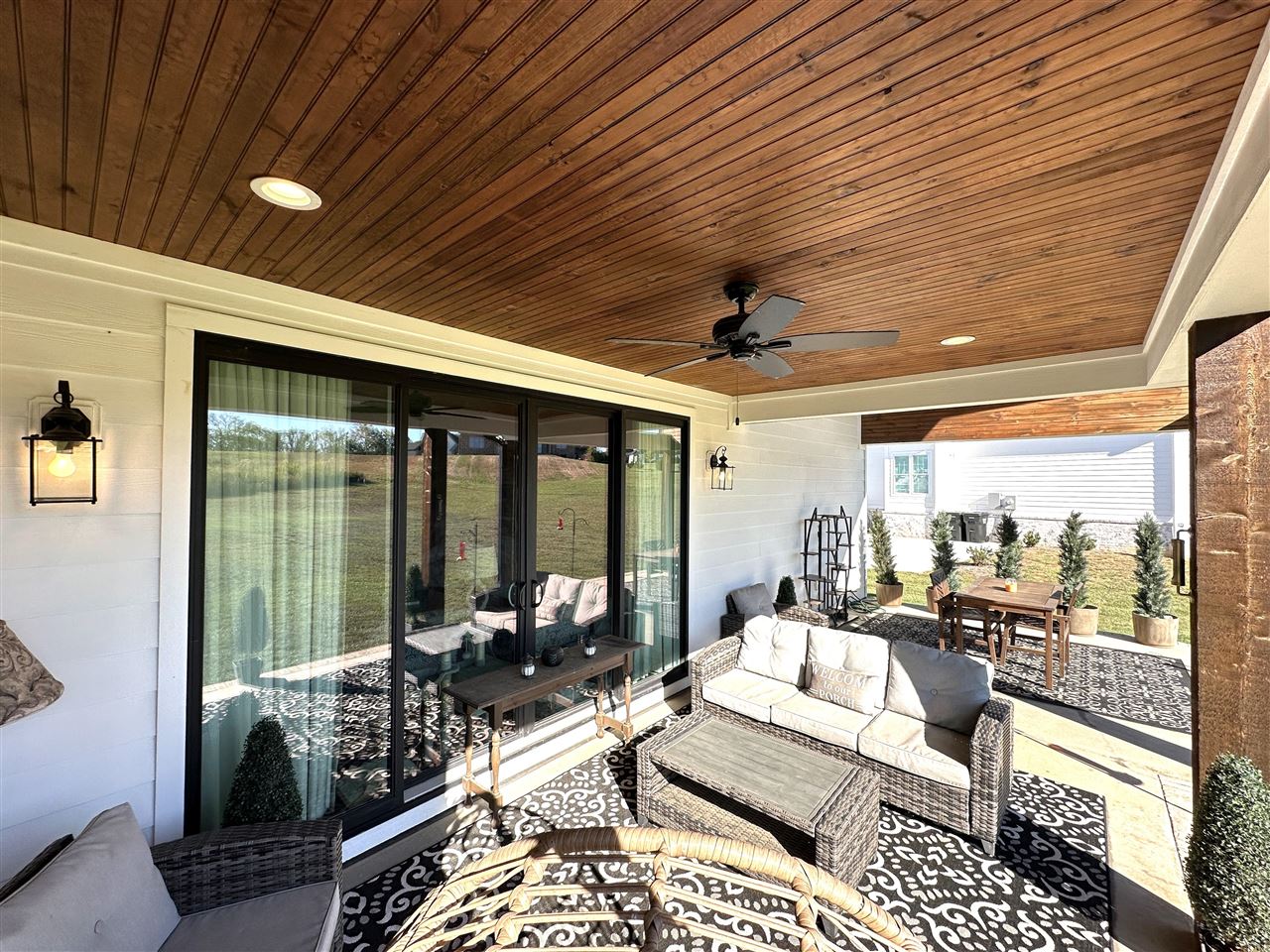 Covered patio with a wood-plank ceiling, wicker seating, and an outdoor dining set.