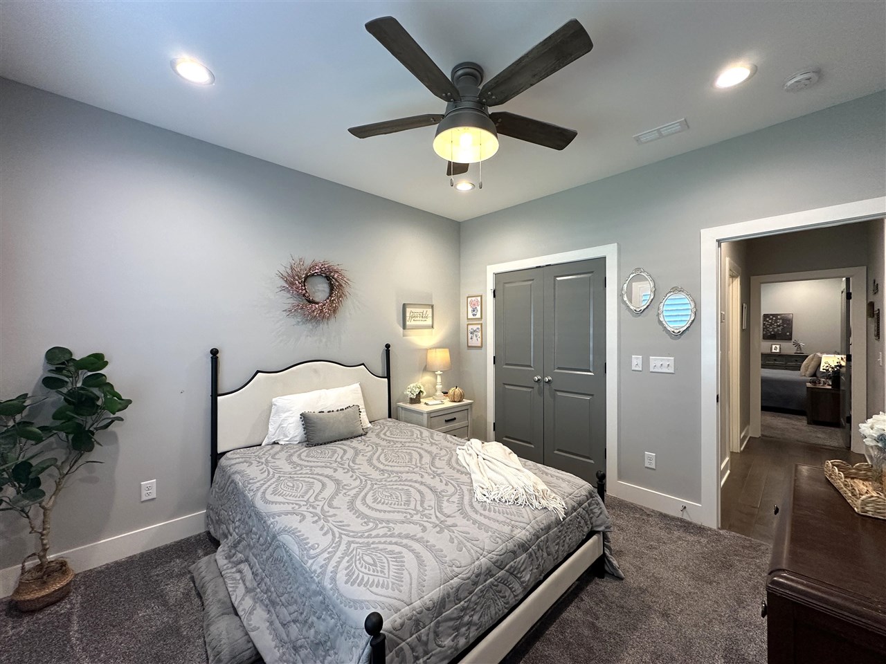 Bedroom with a patterned gray bedspread, dark ceiling fan, and gray double doors.