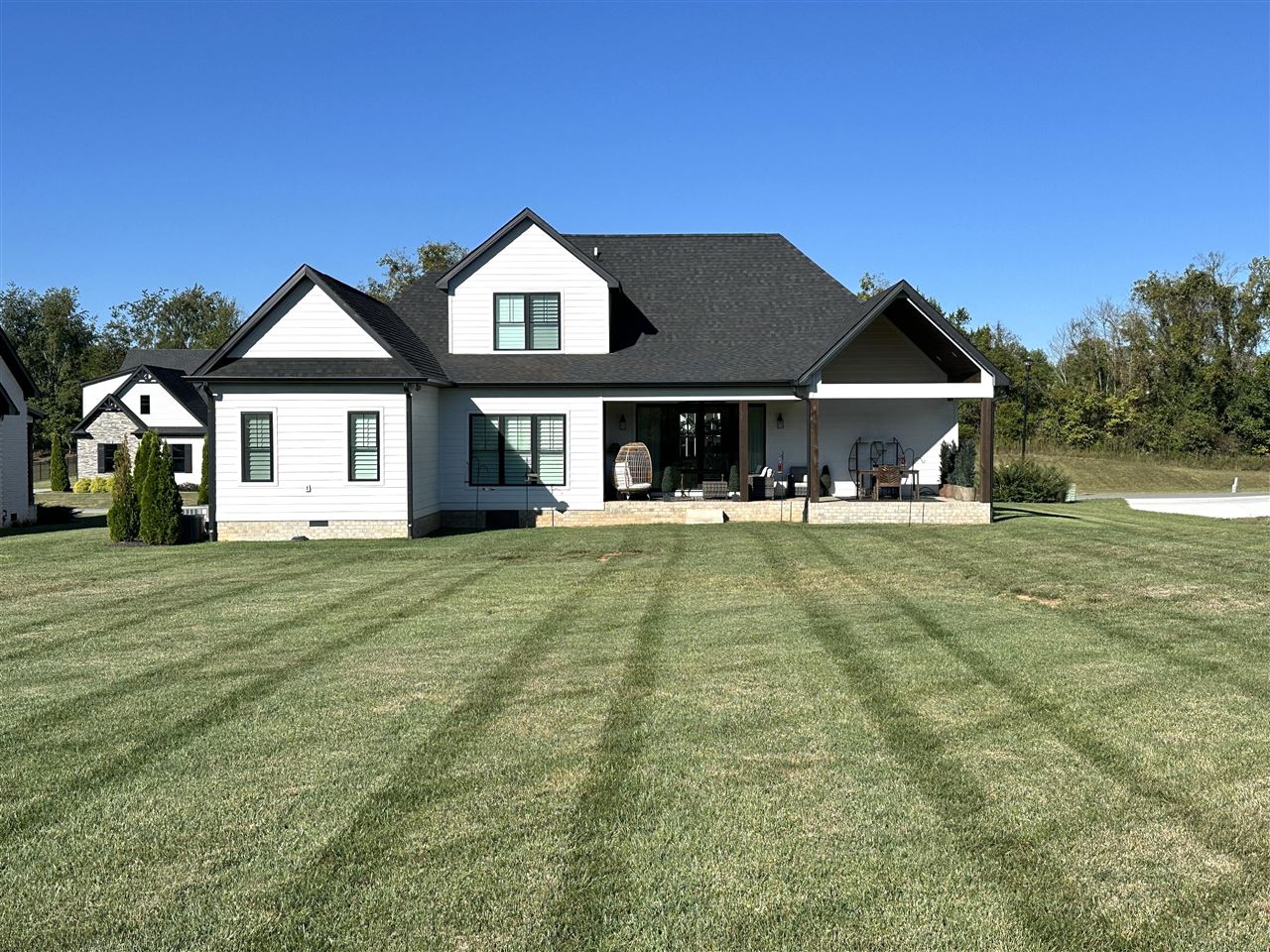 White-sided home with a covered, furnished patio overlooking a broad lawn.