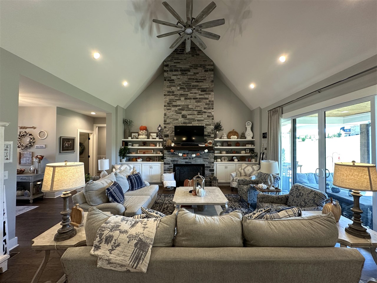 Living room with vaulted ceiling, tall stone fireplace, built-in shelves, and sliding glass doors to a patio.