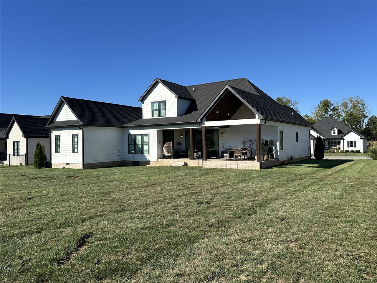 White-sided home with a covered, furnished patio overlooking a broad lawn.