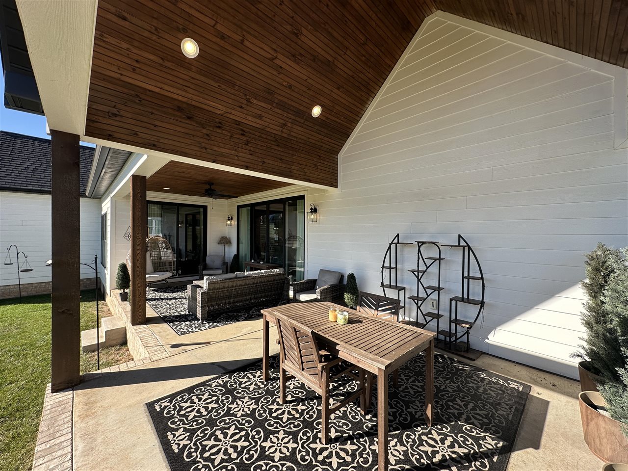 Covered patio with a vaulted wood ceiling, dining set, and lounge seating beside sliding glass doors.