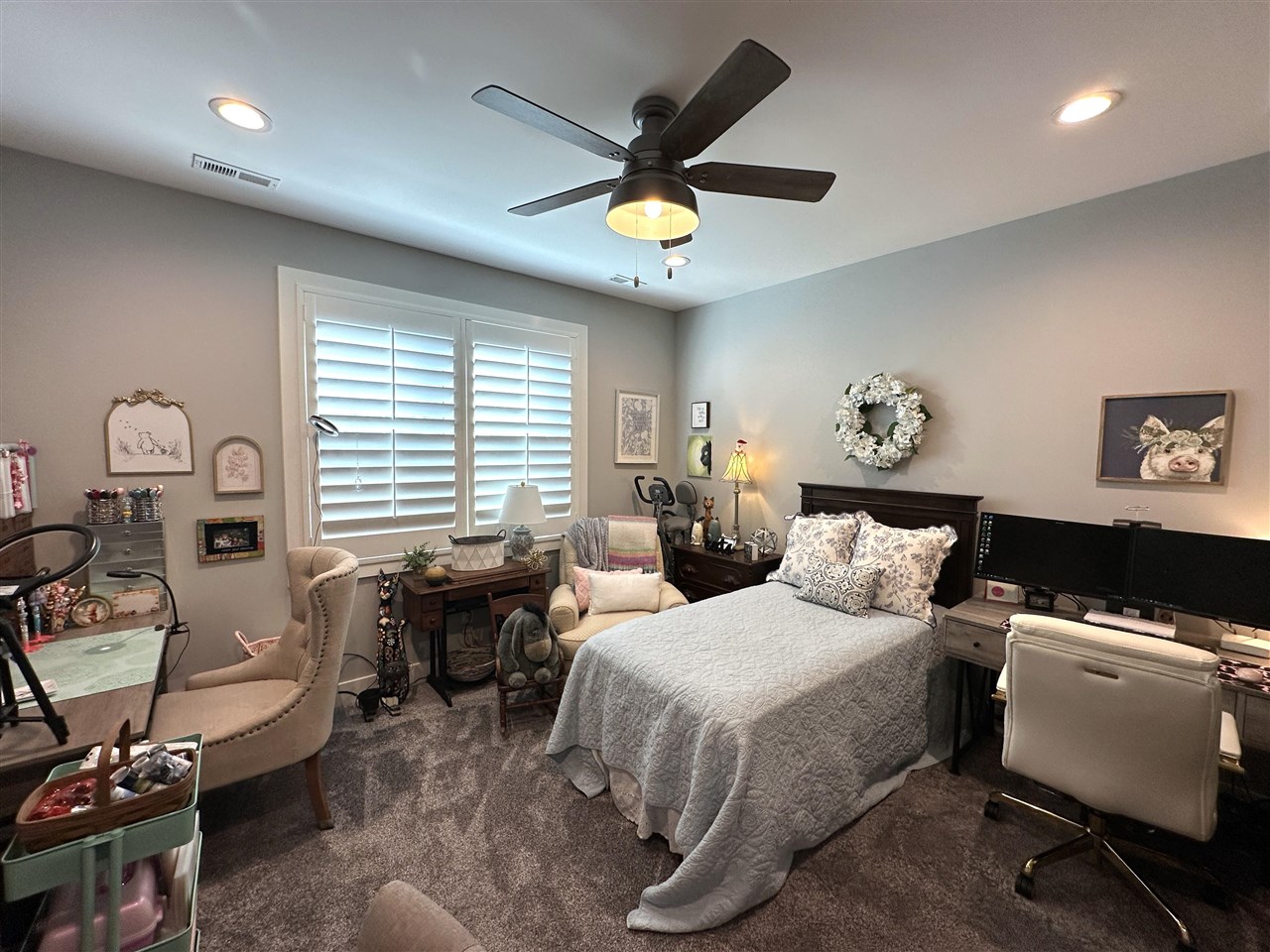 Furnished bedroom with a bed, shuttered windows, ceiling fan, and computer workstation.
