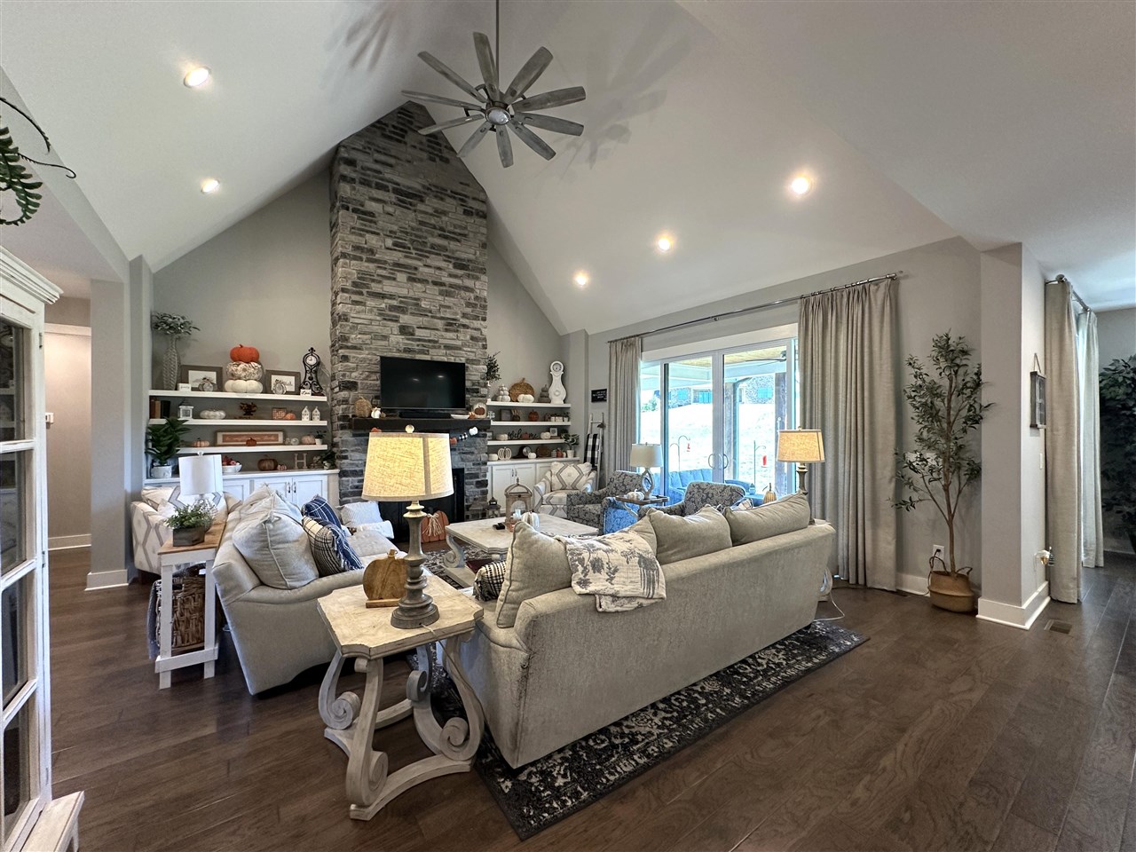 Living room with a vaulted ceiling, stone fireplace, built-in shelves, and sliding glass doors.