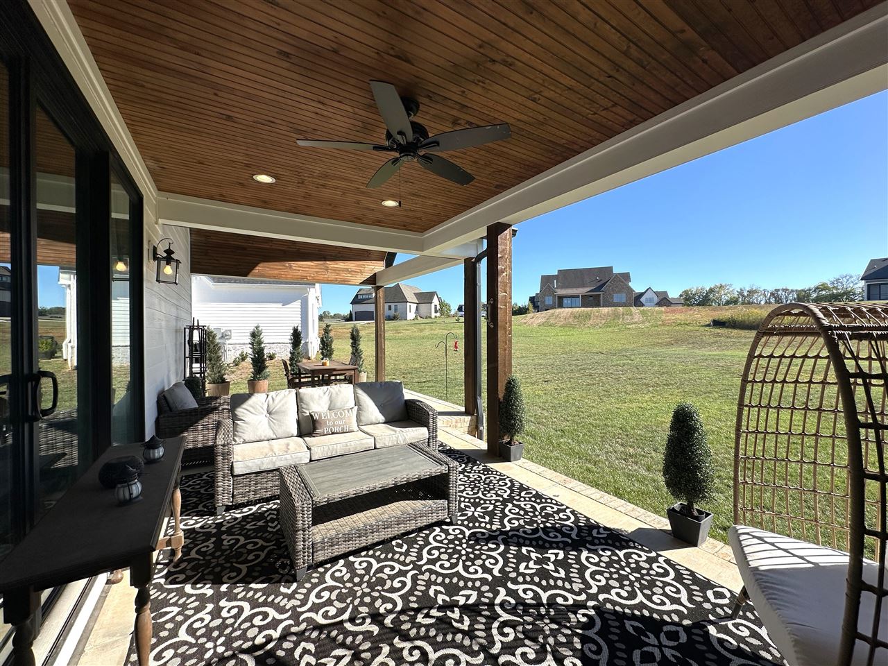 Covered patio with wicker seating and a wood ceiling overlooking a grassy yard.