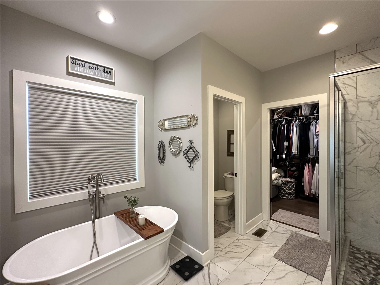 Bathroom with a freestanding soaking tub, marble-look floors, glass shower, and adjoining walk-in closet.