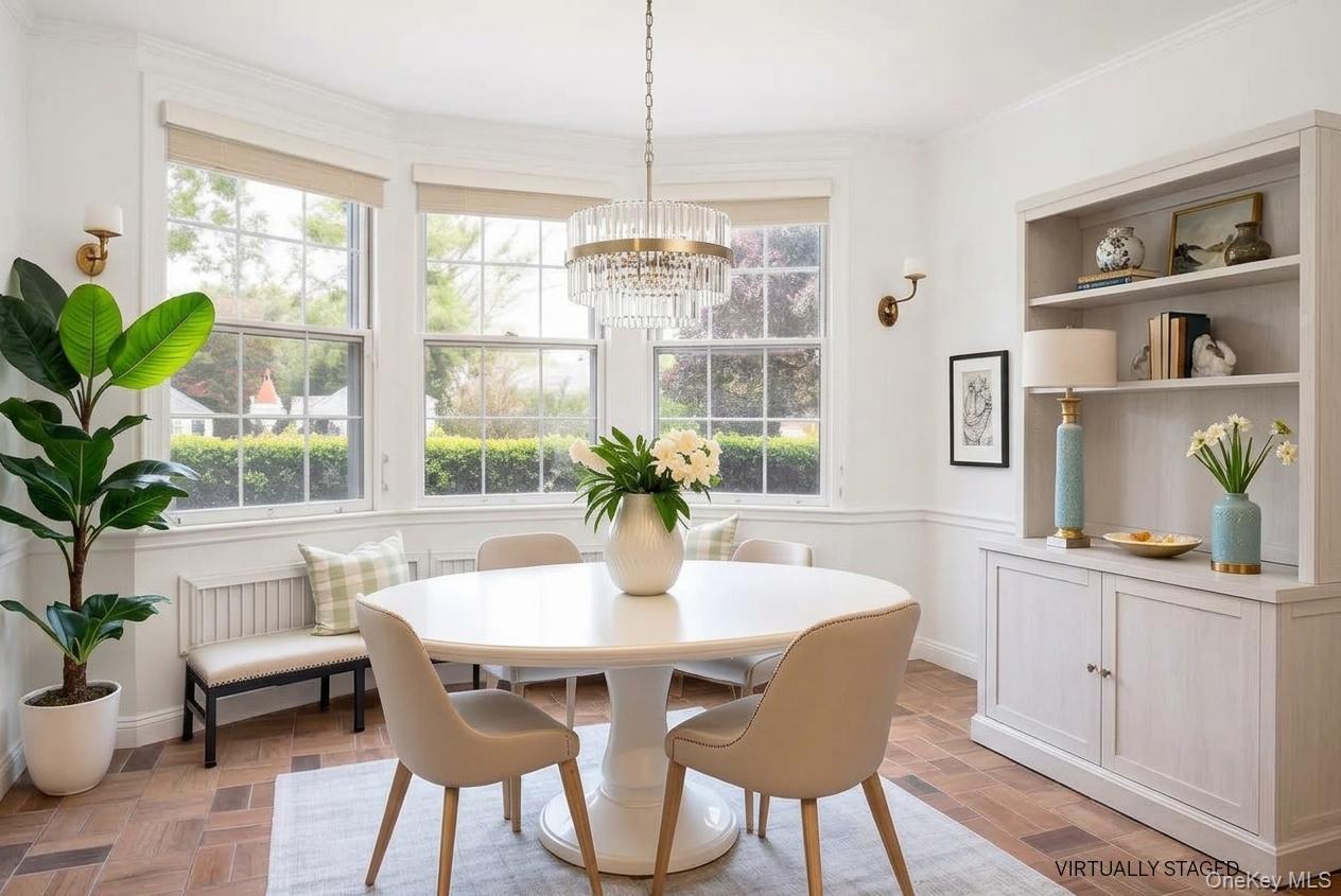 Dining room with a round white table, crystal chandelier, built-in cabinetry, and three bright windows.