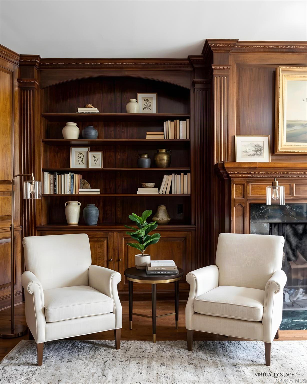 Living room with a dark wood bookcase, two cream armchairs, and an ornate fireplace.