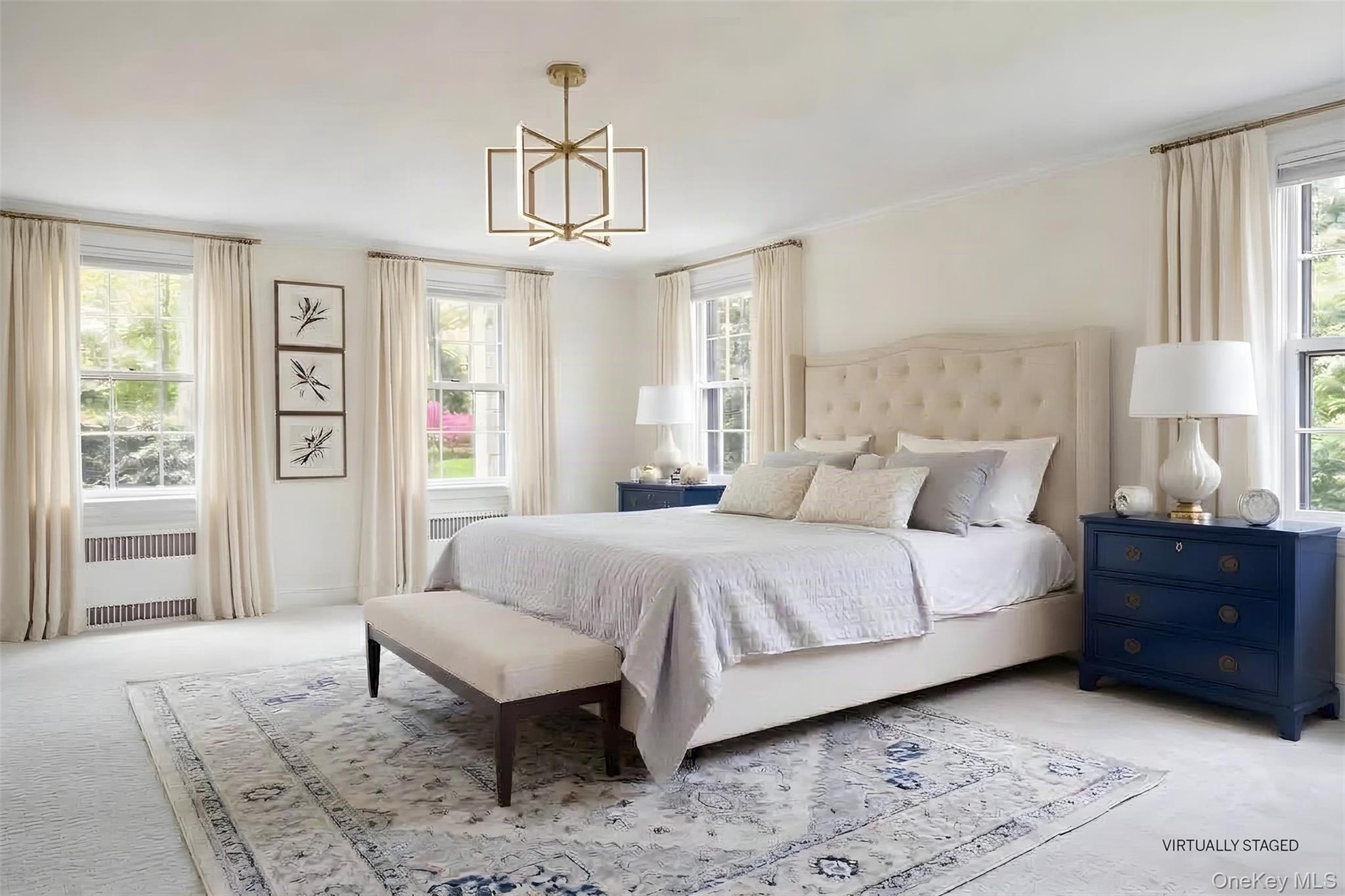 Virtually staged bedroom with a tufted bed, blue dressers, and bright windows.