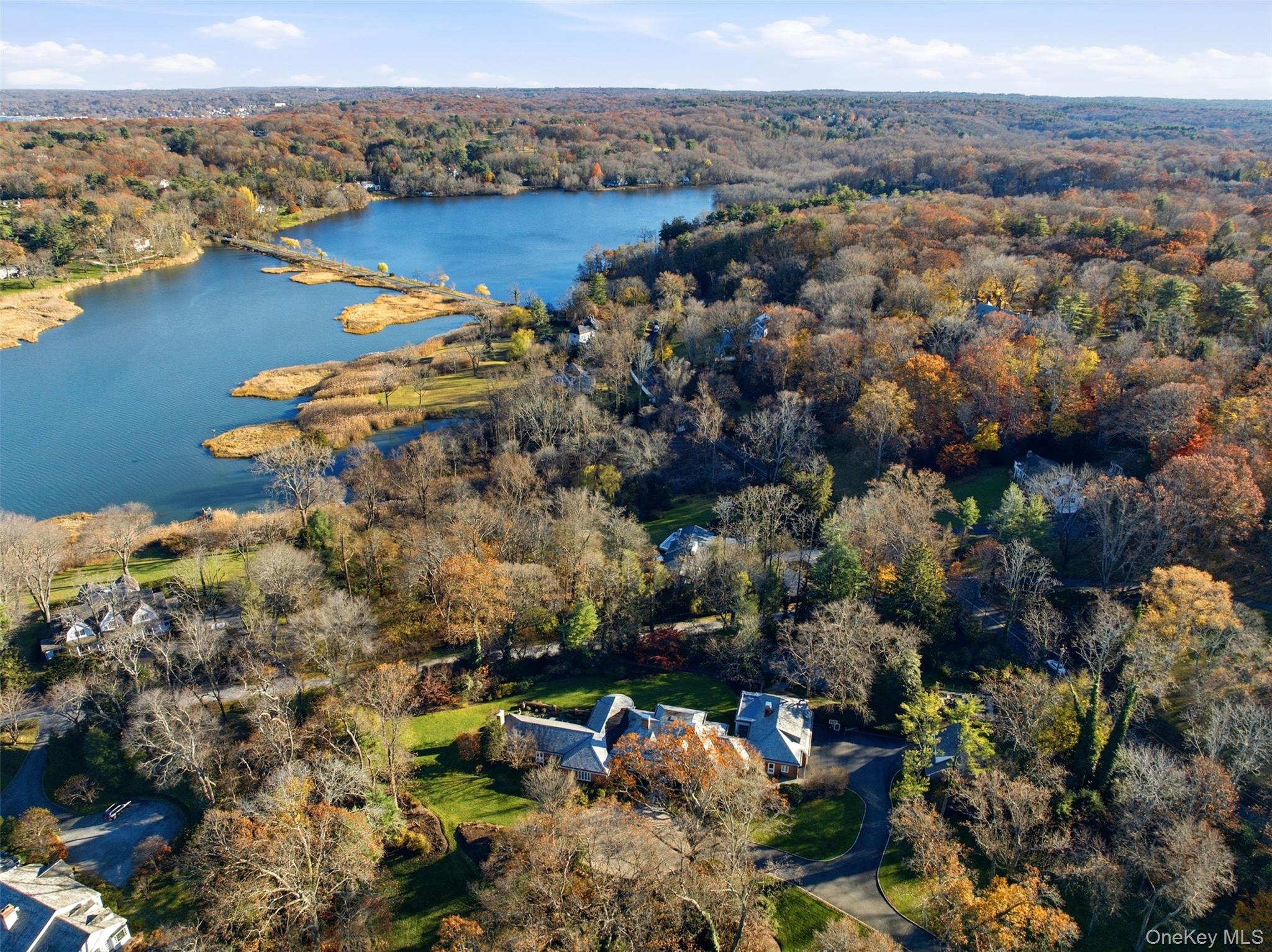 Aerial view of a large home amid autumn trees beside a pond.