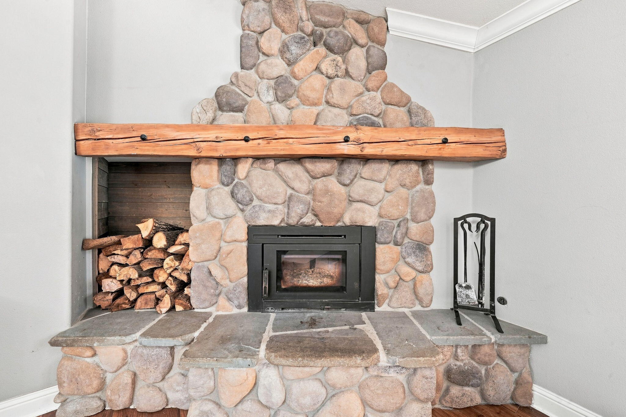 Stone fireplace with a heavy timber mantel, wood-burning insert, and stacked firewood.