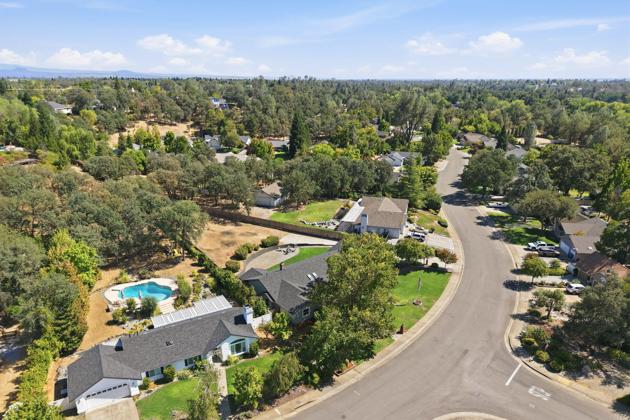 Aerial view of a home with a swimming pool beside a curving residential street.