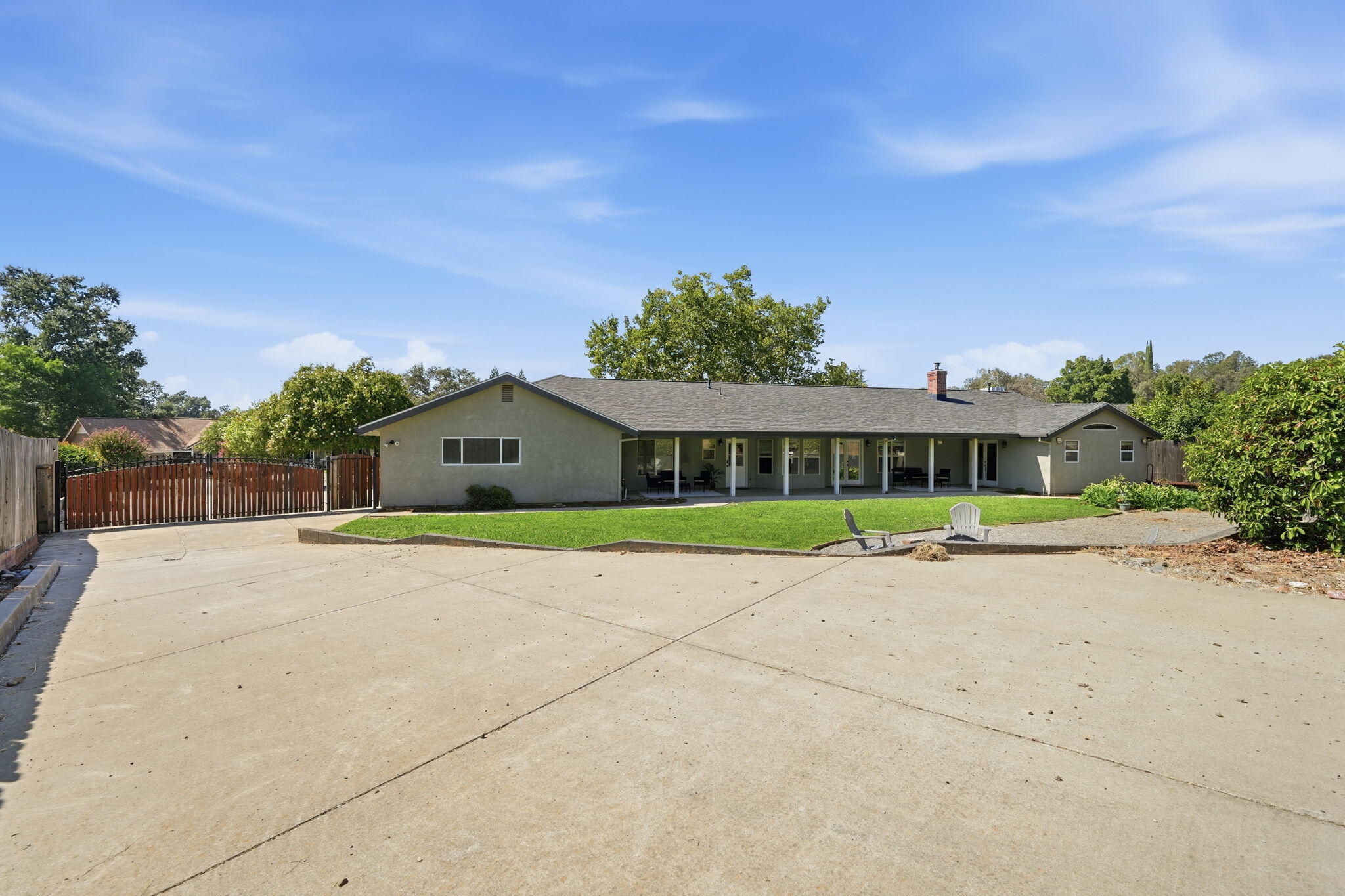 Rear of a single-story home with a covered patio, broad concrete yard, and fenced lawn.