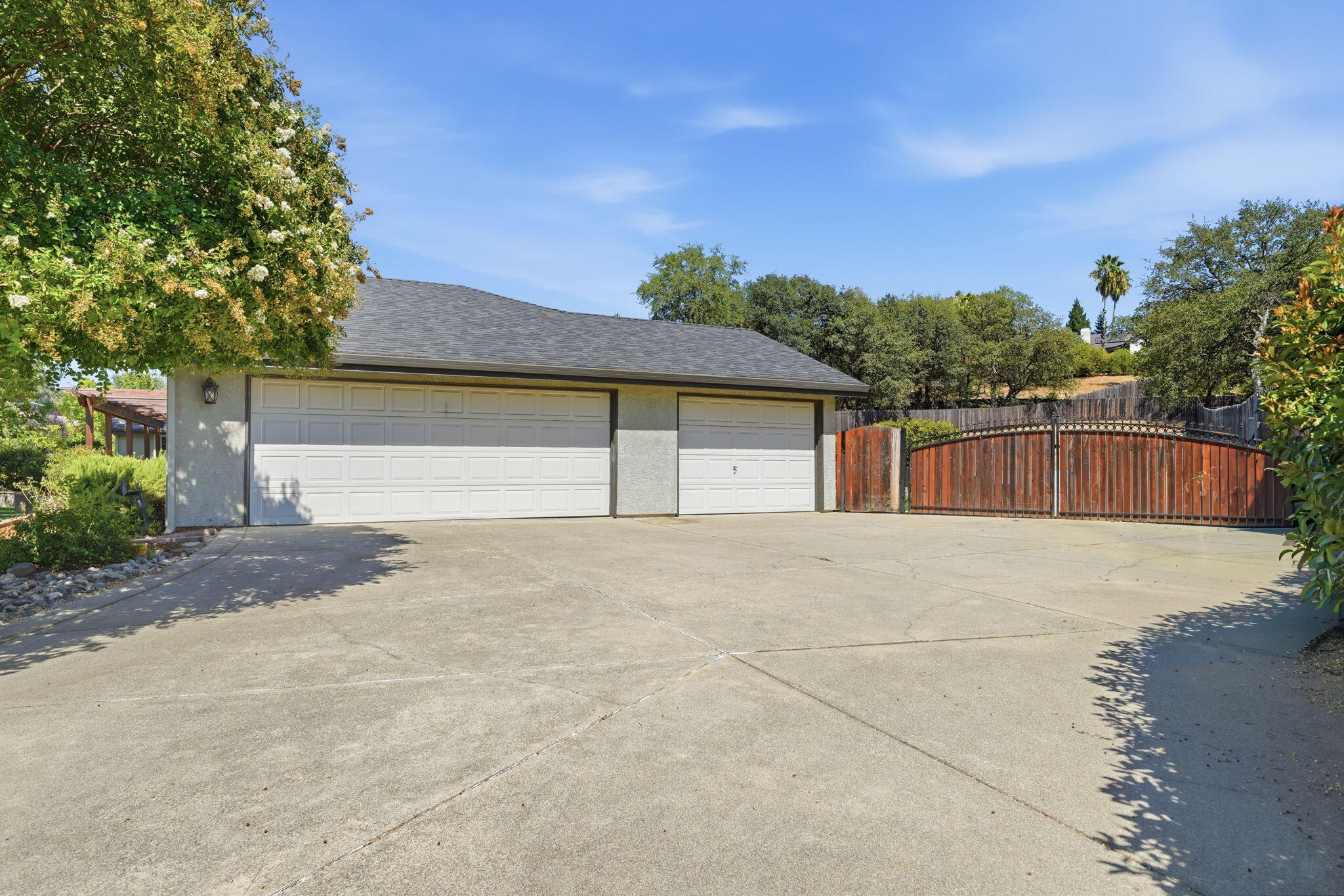 Detached three-car garage beside a wide concrete driveway and arched wooden gate.