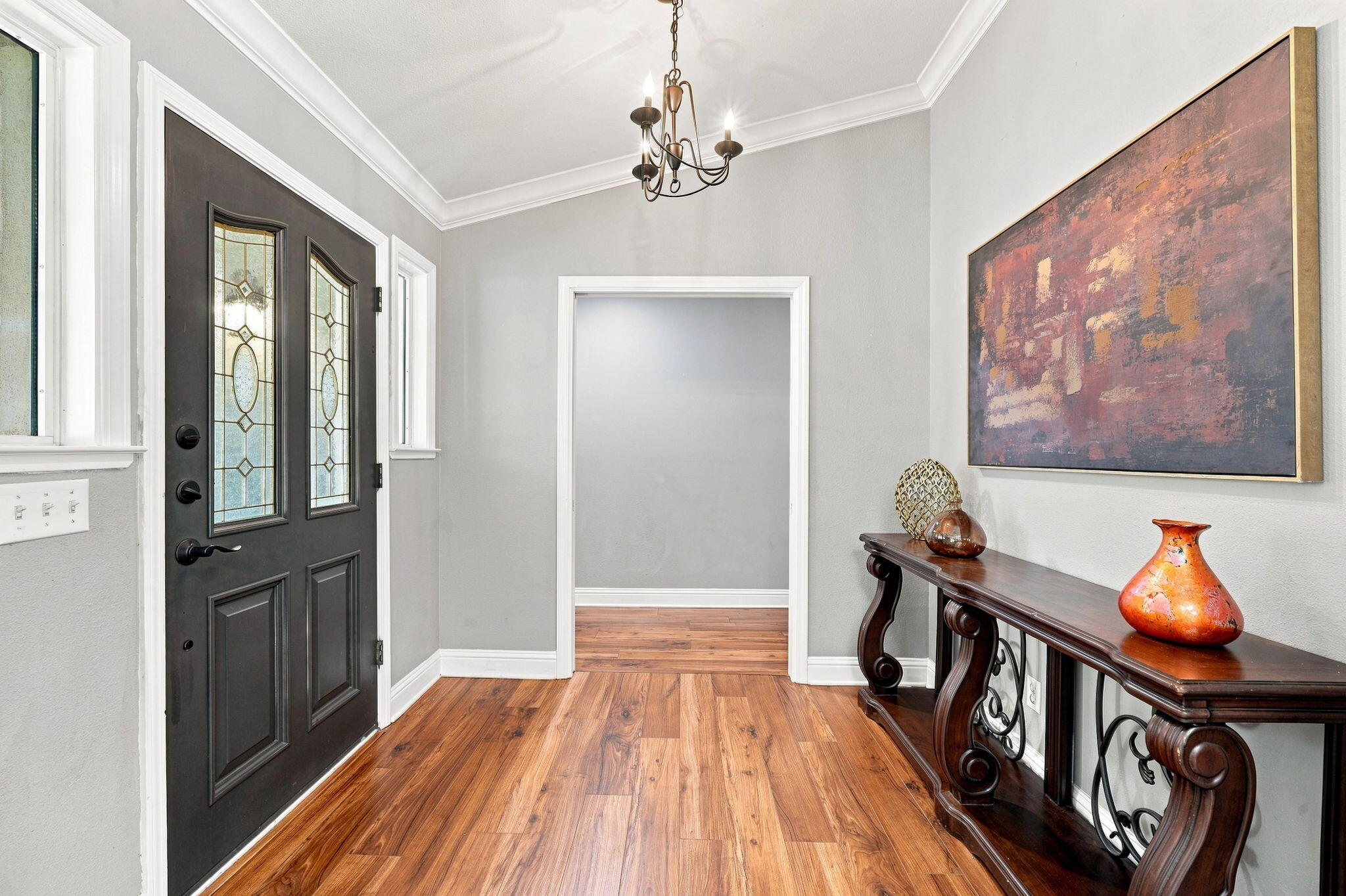 Entry foyer with a black glass-paneled front door, warm wood floors, and a carved console table.