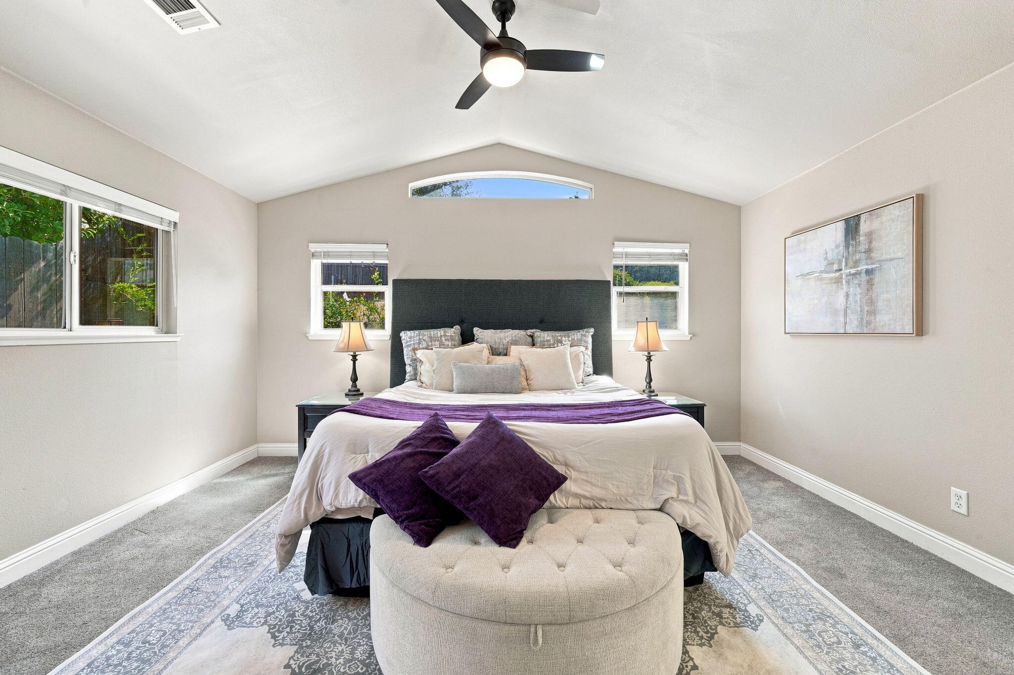 Staged bedroom with a king bed, purple accents, and a high vaulted ceiling with a ceiling fan.
