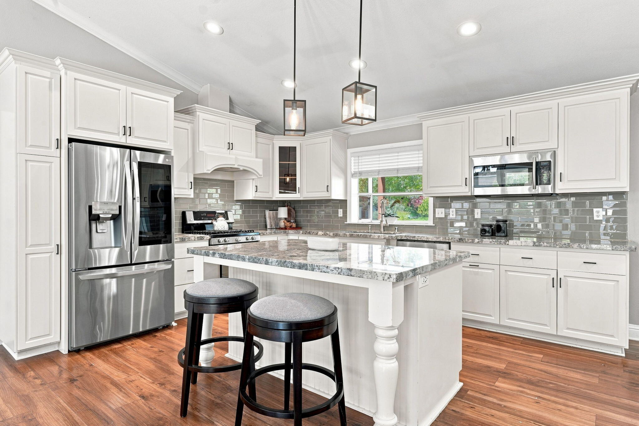 Bright kitchen with a large granite island, white cabinetry, stainless steel appliances, and hardwood floors.