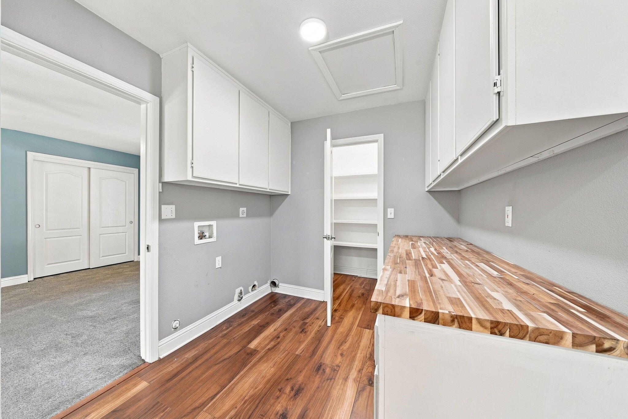 Laundry room with white cabinets, washer hookups, open shelving, and a butcher-block folding counter.