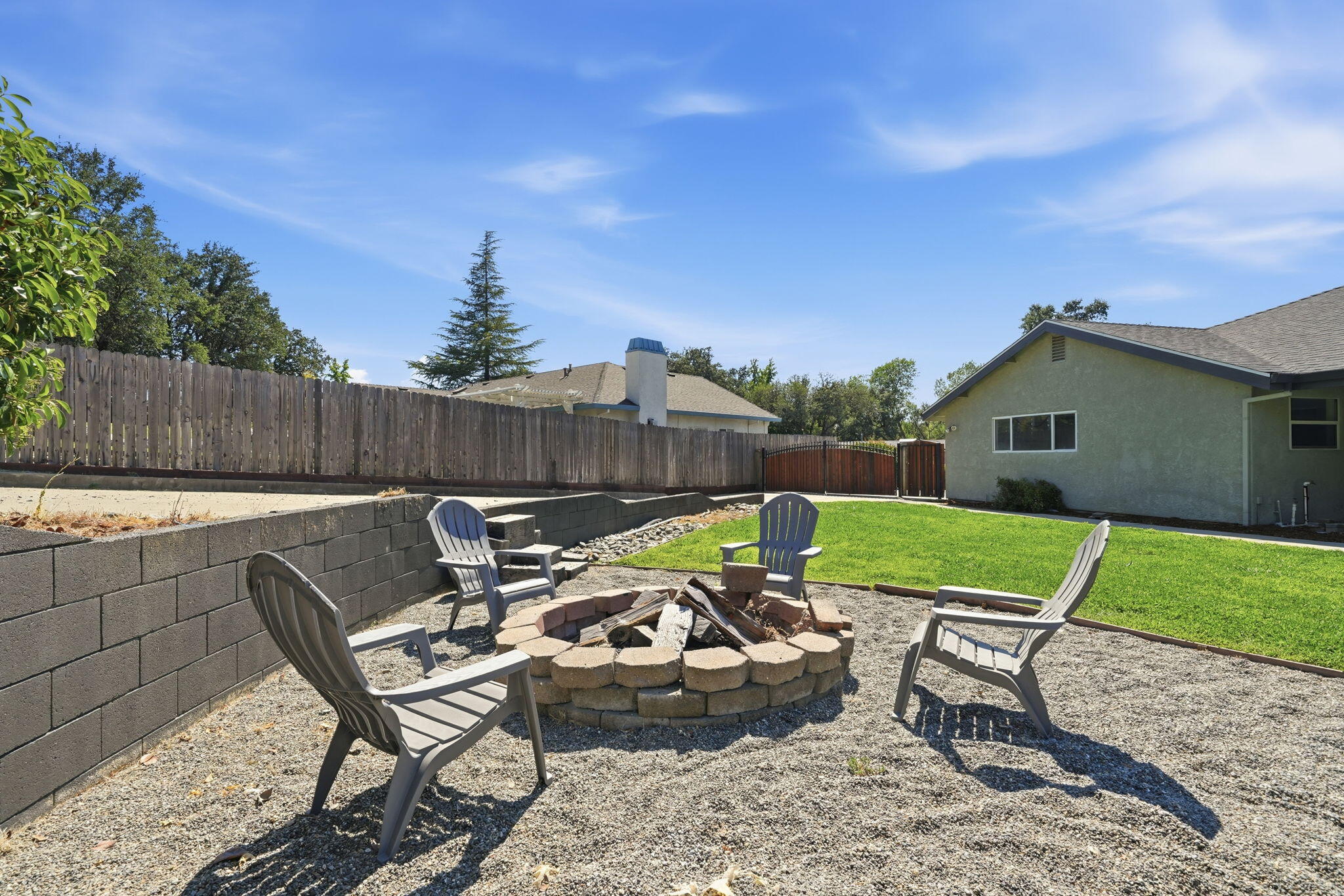 Backyard patio with a stone fire pit, Adirondack chairs, gravel, and a small lawn.