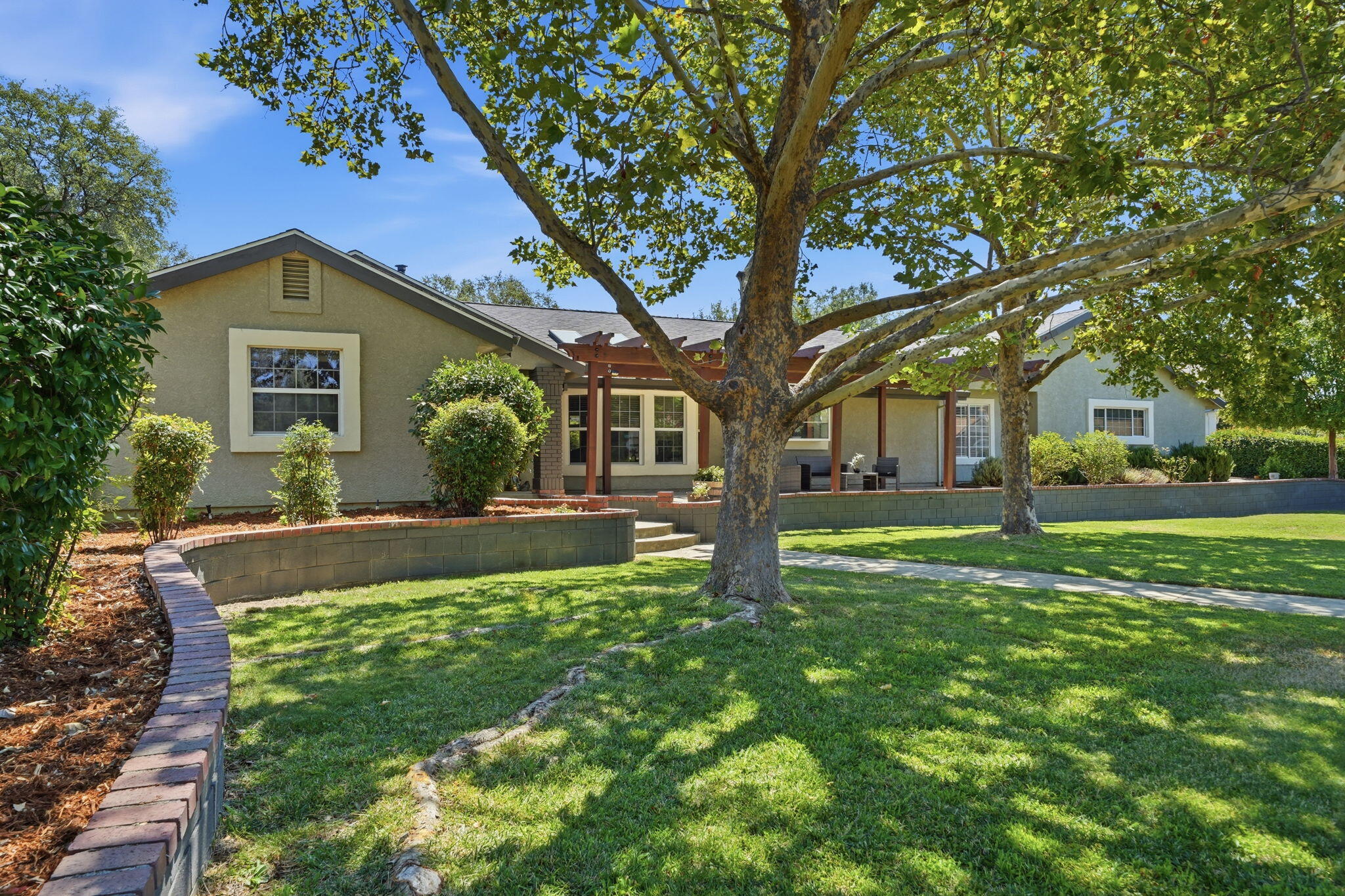 Home’s rear exterior with a covered patio, mature shade trees, and a landscaped lawn.