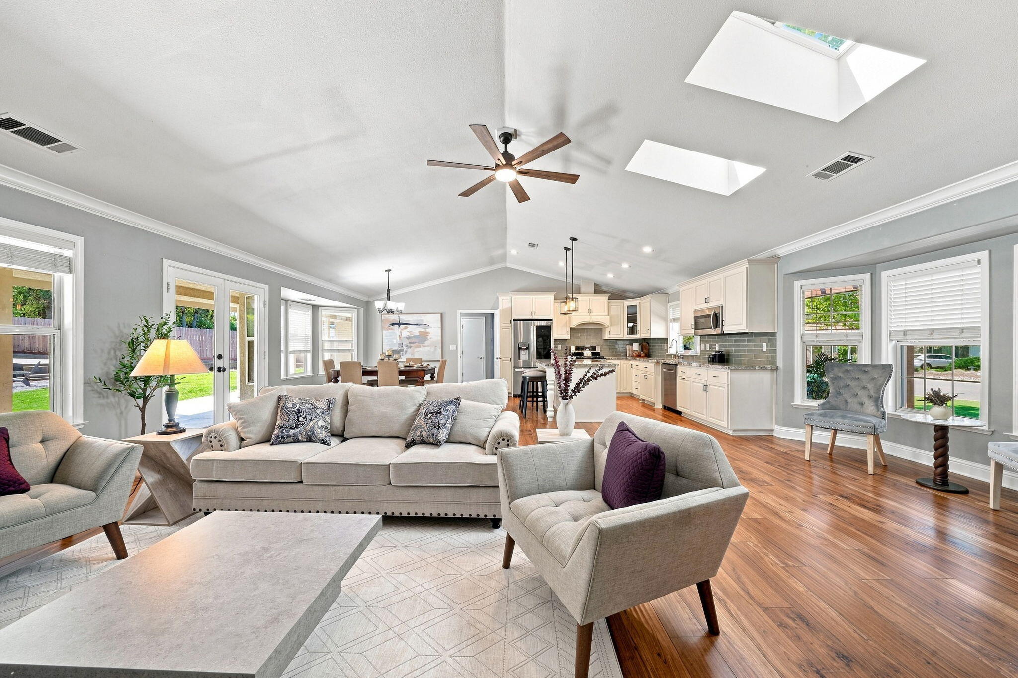 Open-plan living room and kitchen with vaulted ceiling, skylights, and wood flooring.