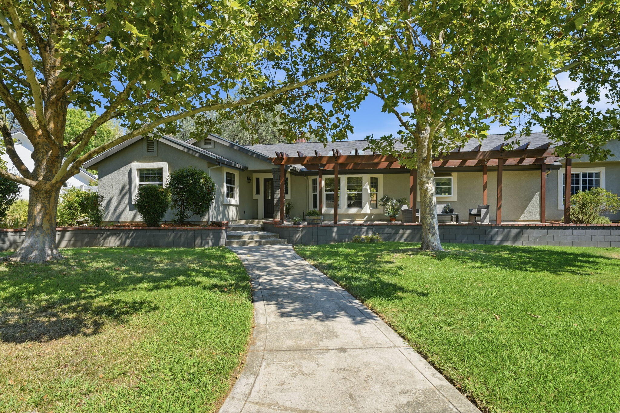 Single-story home with a covered pergola patio, shaded lawn, and a walkway leading to the entrance.