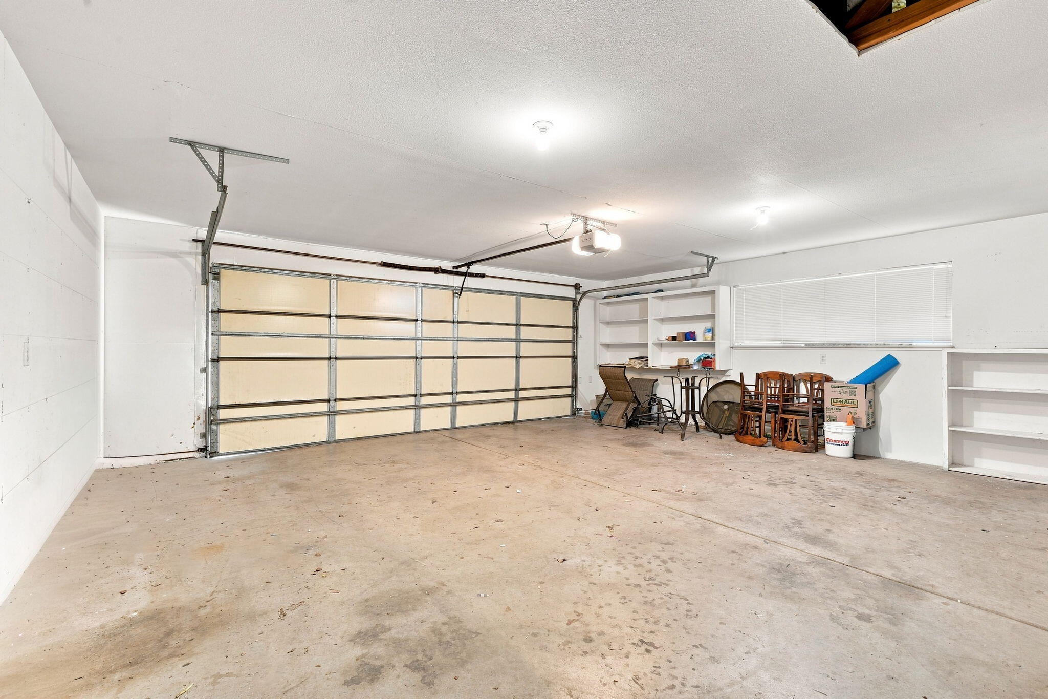 Garage with a large sectional door, concrete floor, and shelving with stored furniture.