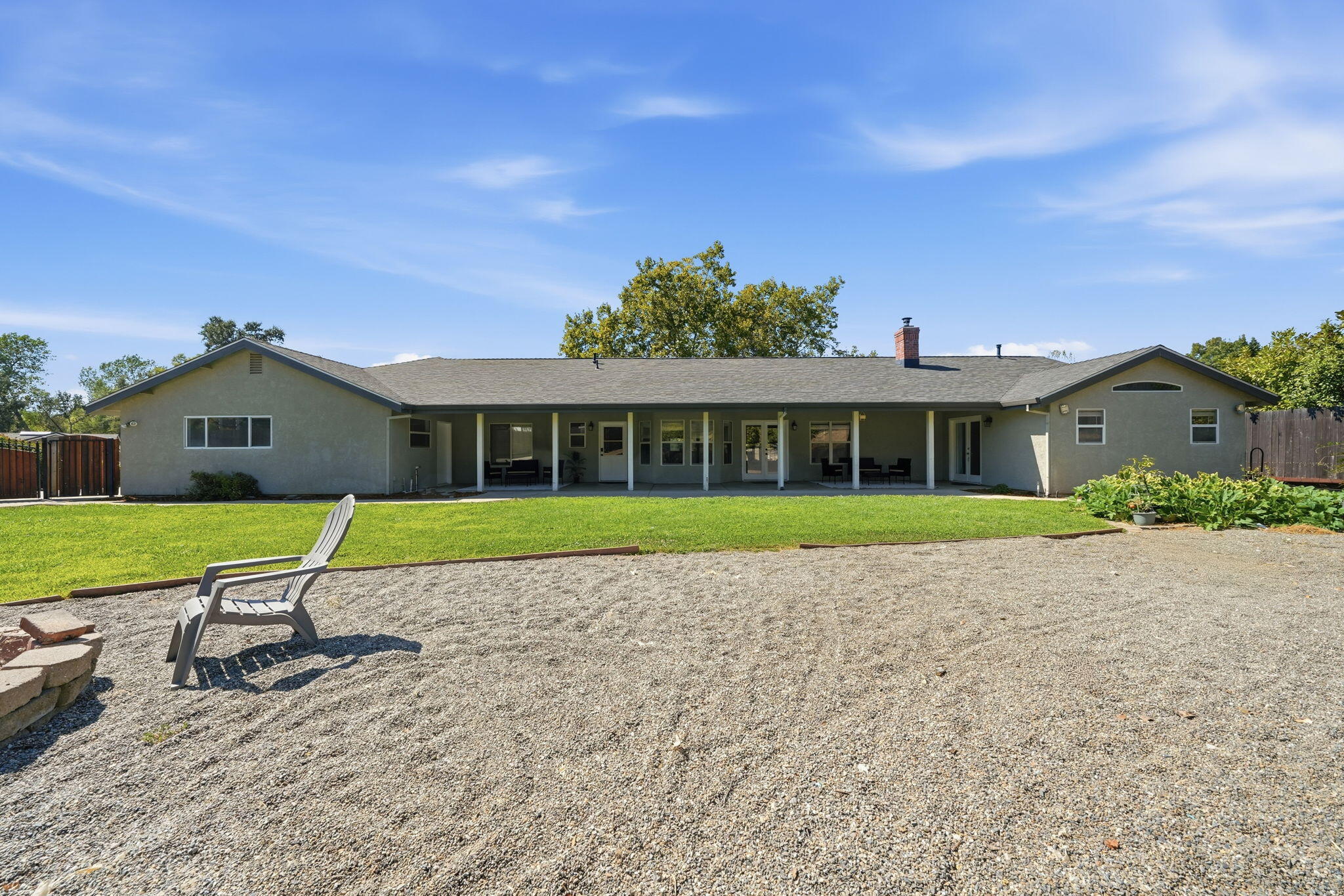 Rear exterior of a single-story home with a covered patio, lawn, and gravel seating area.