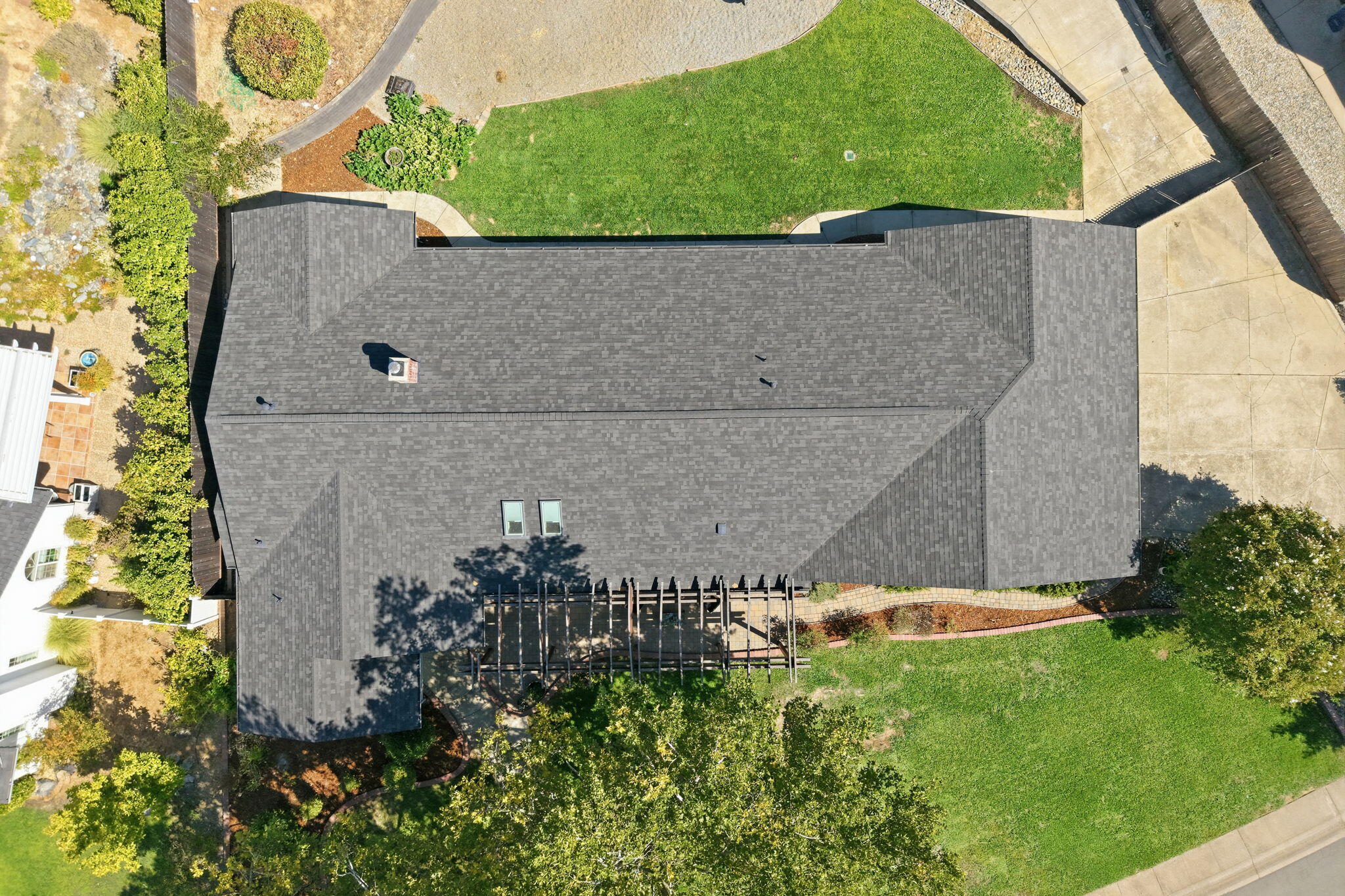Aerial view of a home’s gray shingle roof, lawn, and backyard pergola.